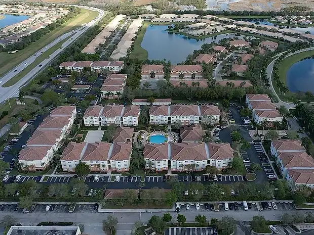 Aerial view of a townhome community with terracotta tile roofs beside a lake
